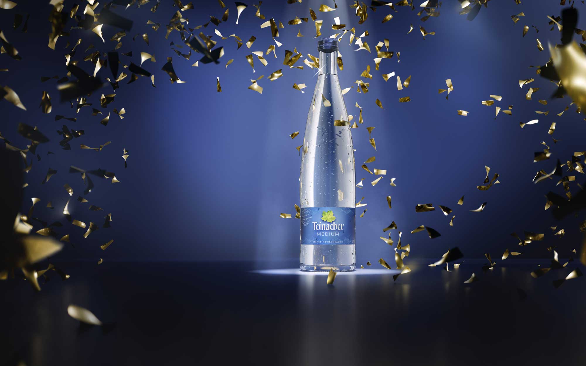 Teinacher Genussflasche blauer Hintergrund mit Goldkonfetti